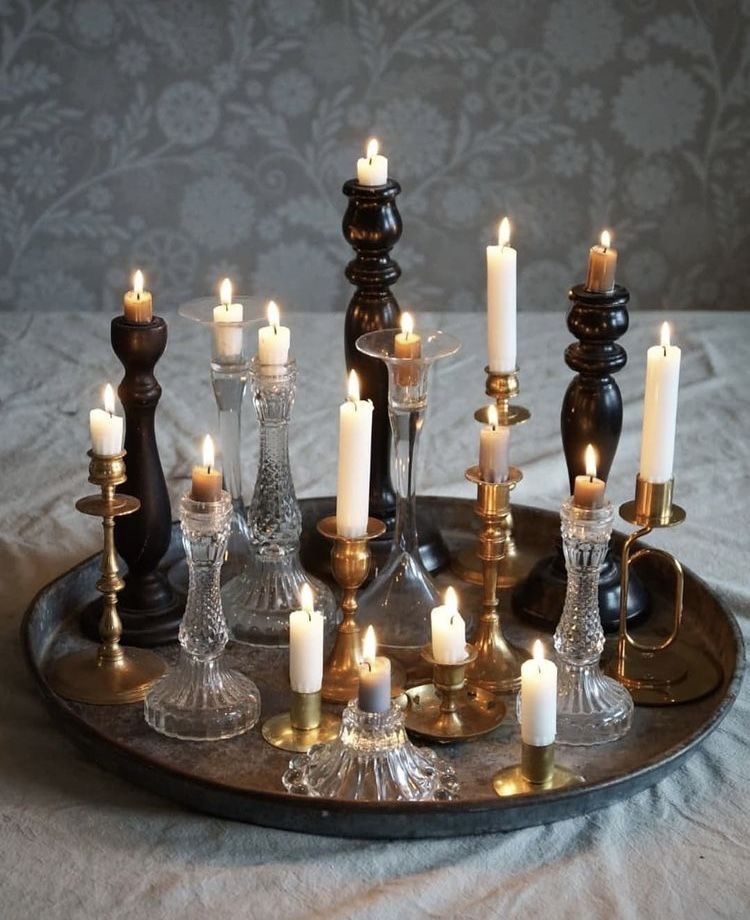 Silver platter holding a collection of candles on top of black, gold, and clear candle holders. The candles are all different heights.
