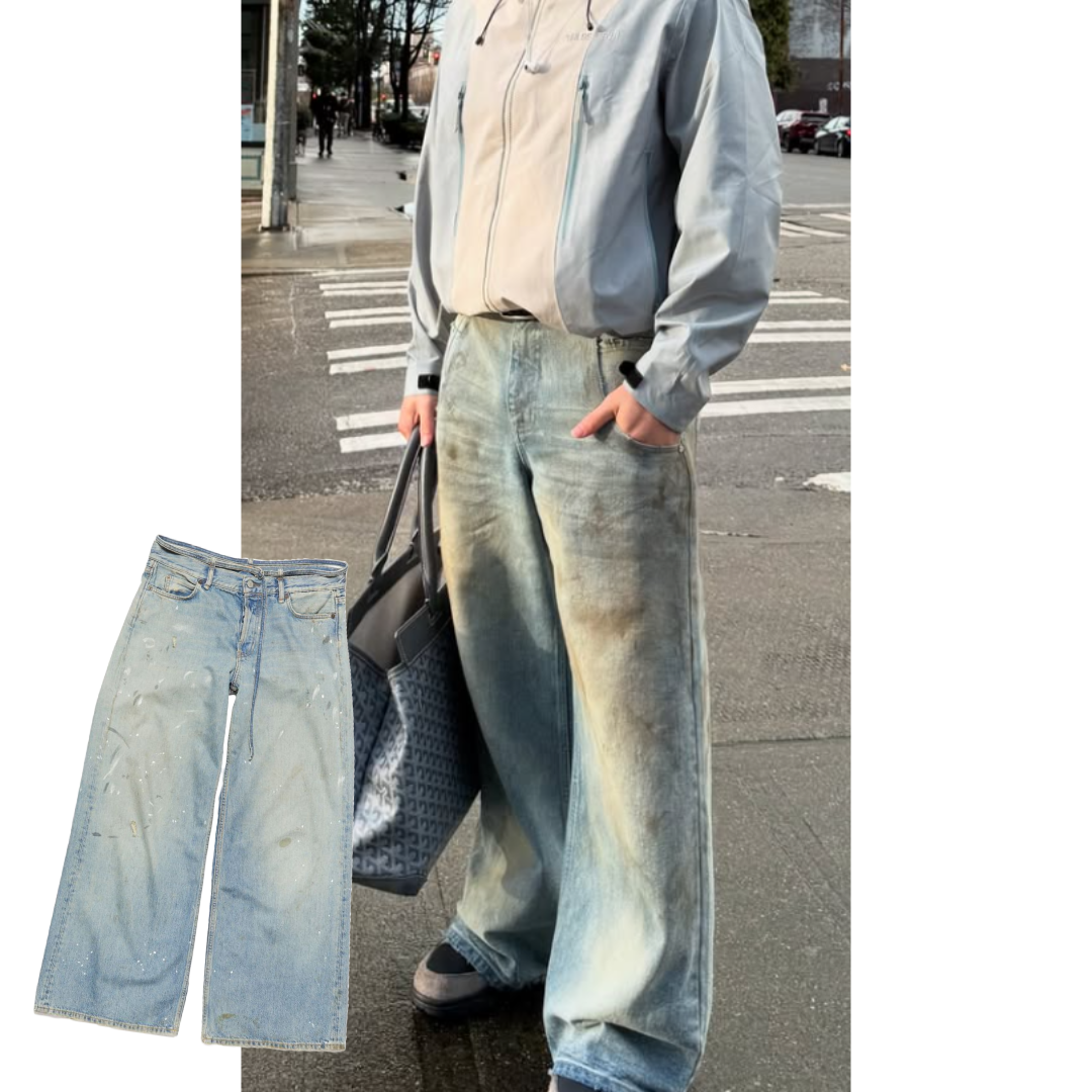 A screenshot of a picture of a man posing in front of a crosswalk. The image is cropped from the deck down to showcase the outfit. The man is wear a light blue and white windbreaker jacket with a light wash pair of baggy jeans that has stains on it. He is carrying a large blue tote bag