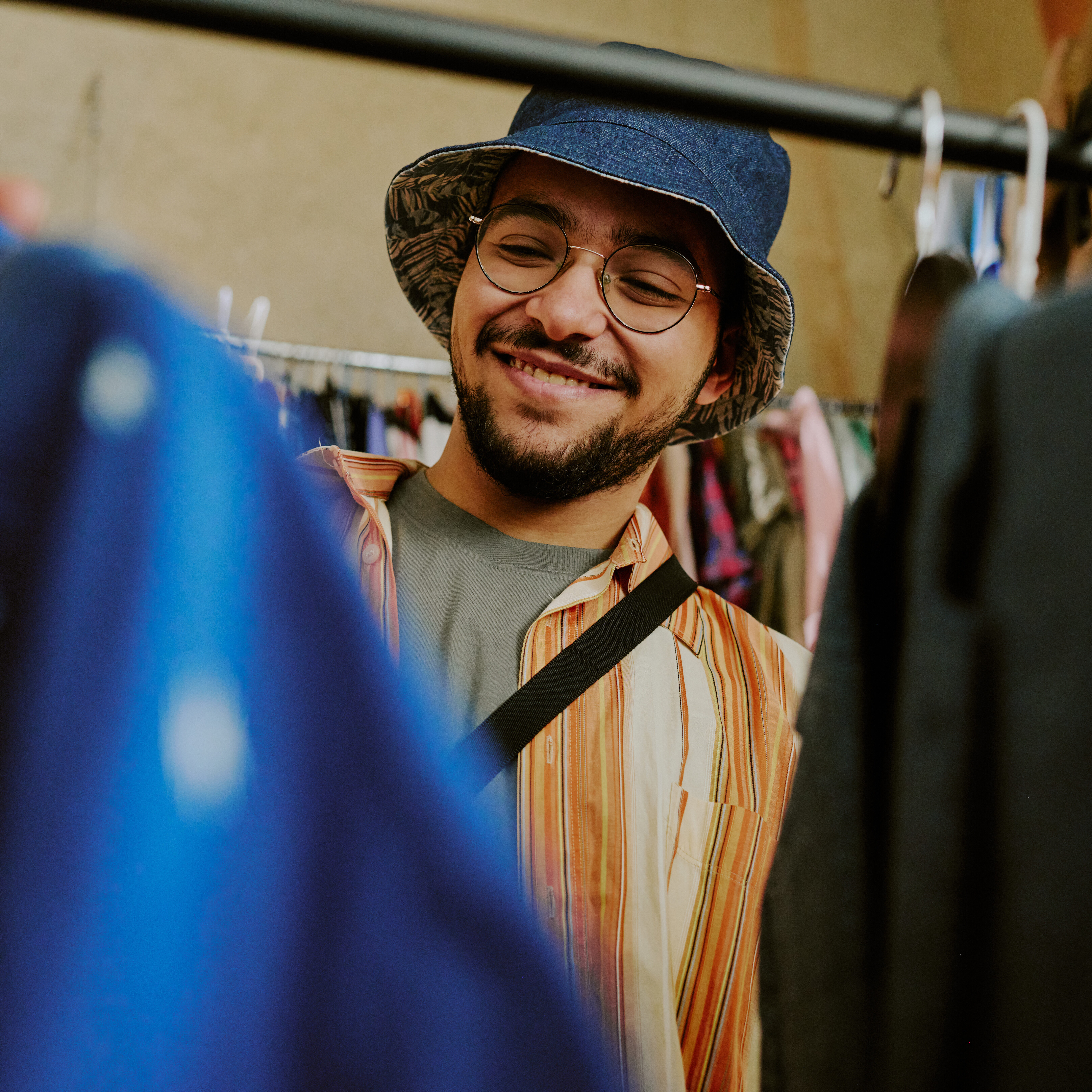 Image of person wearing a hat looking through a clothing rack.