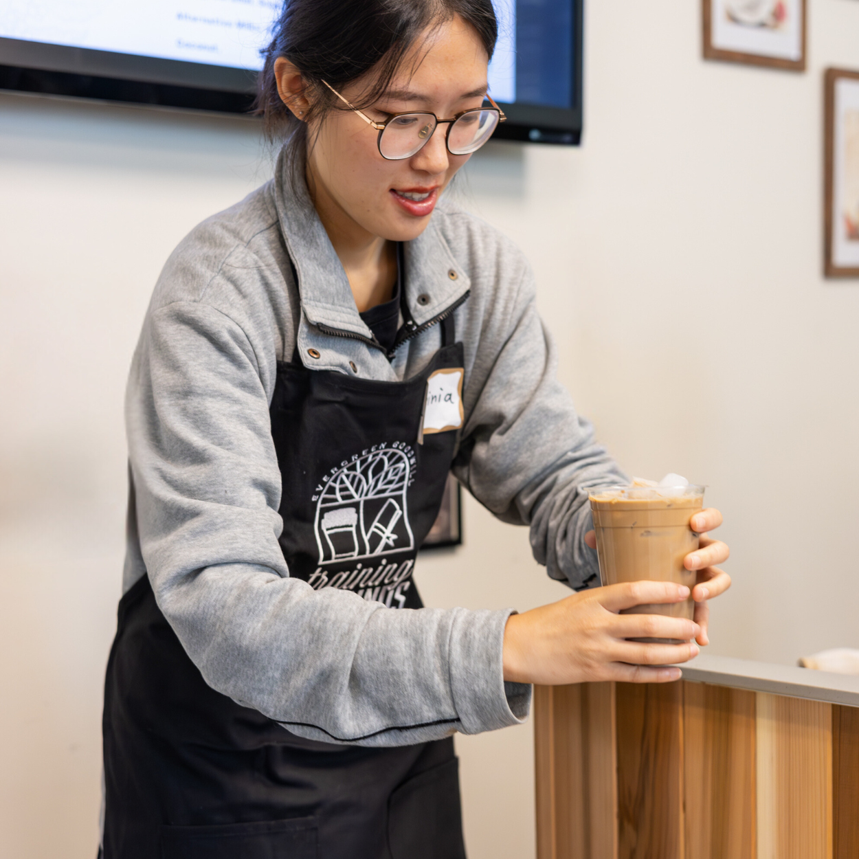 barista at evergreen goodwill serving an iced latte