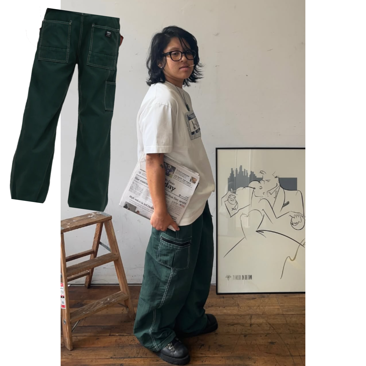A person standing, posing sideways. They are wearing black frame glasses, a white graphic t-shirt, and baggy green pants.