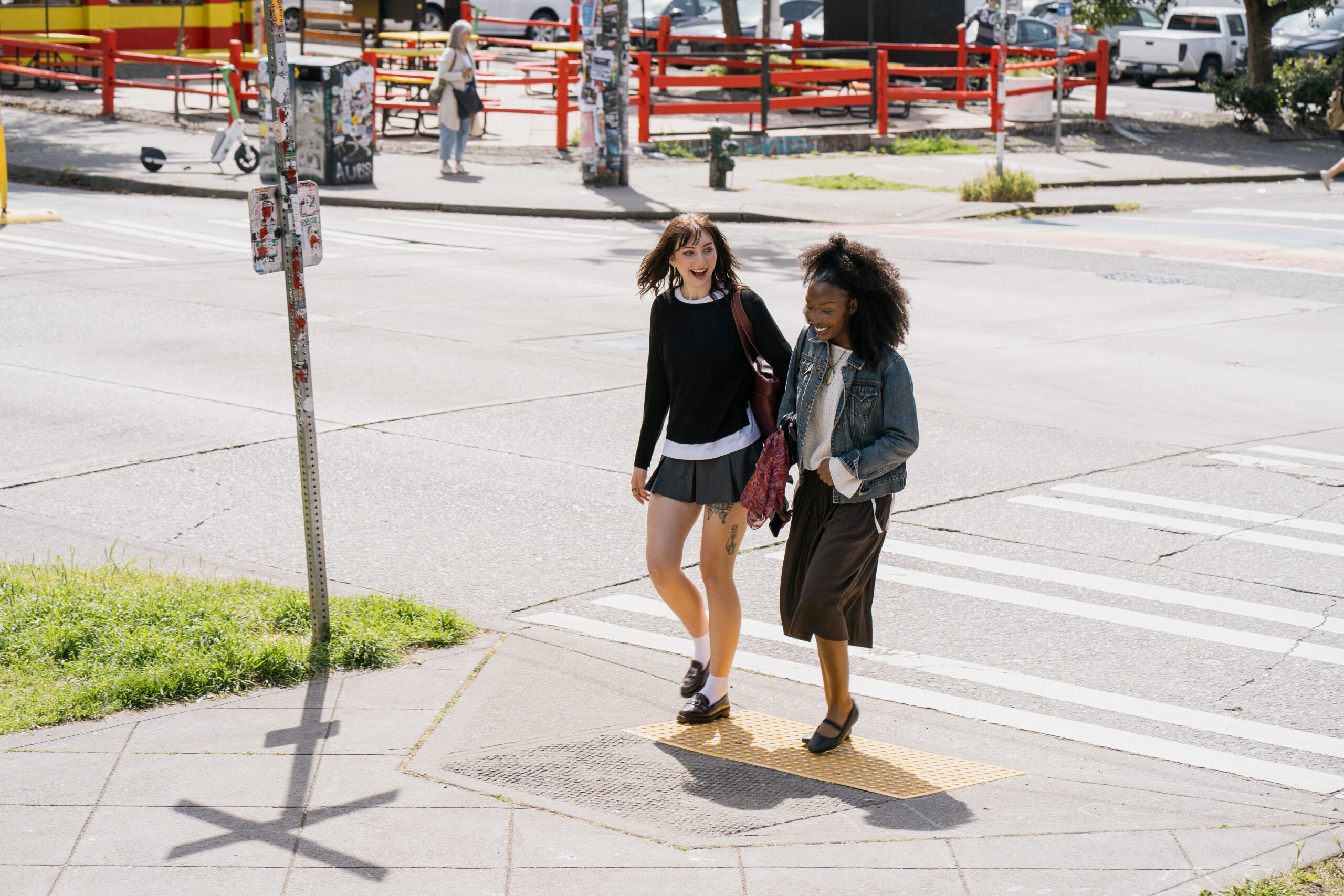 Image of two people walking down a crosswalk wearing summer outfits.