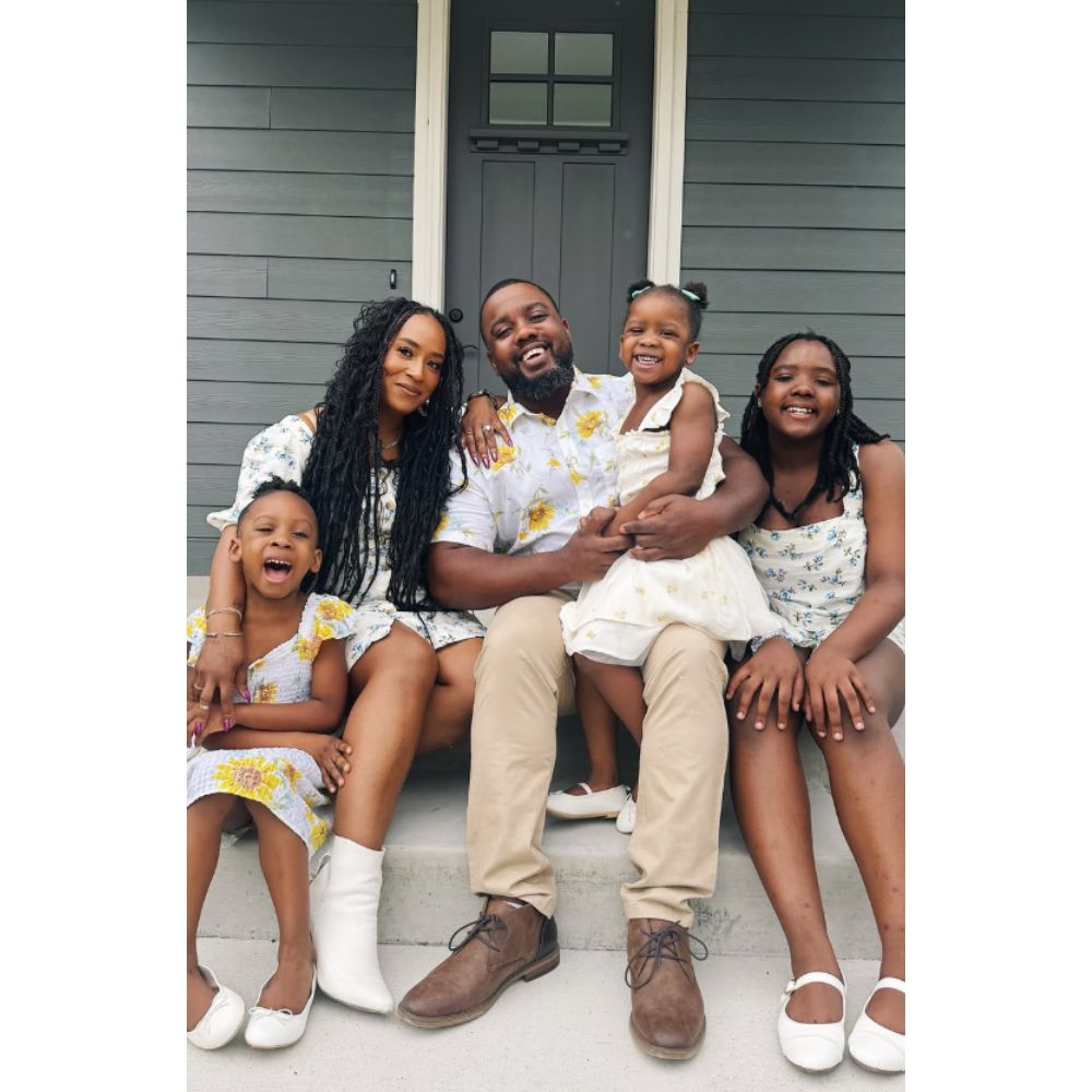 A photo of Tash Haynes with her husband and three daughters. They are sitting together on the floor in front of a door.