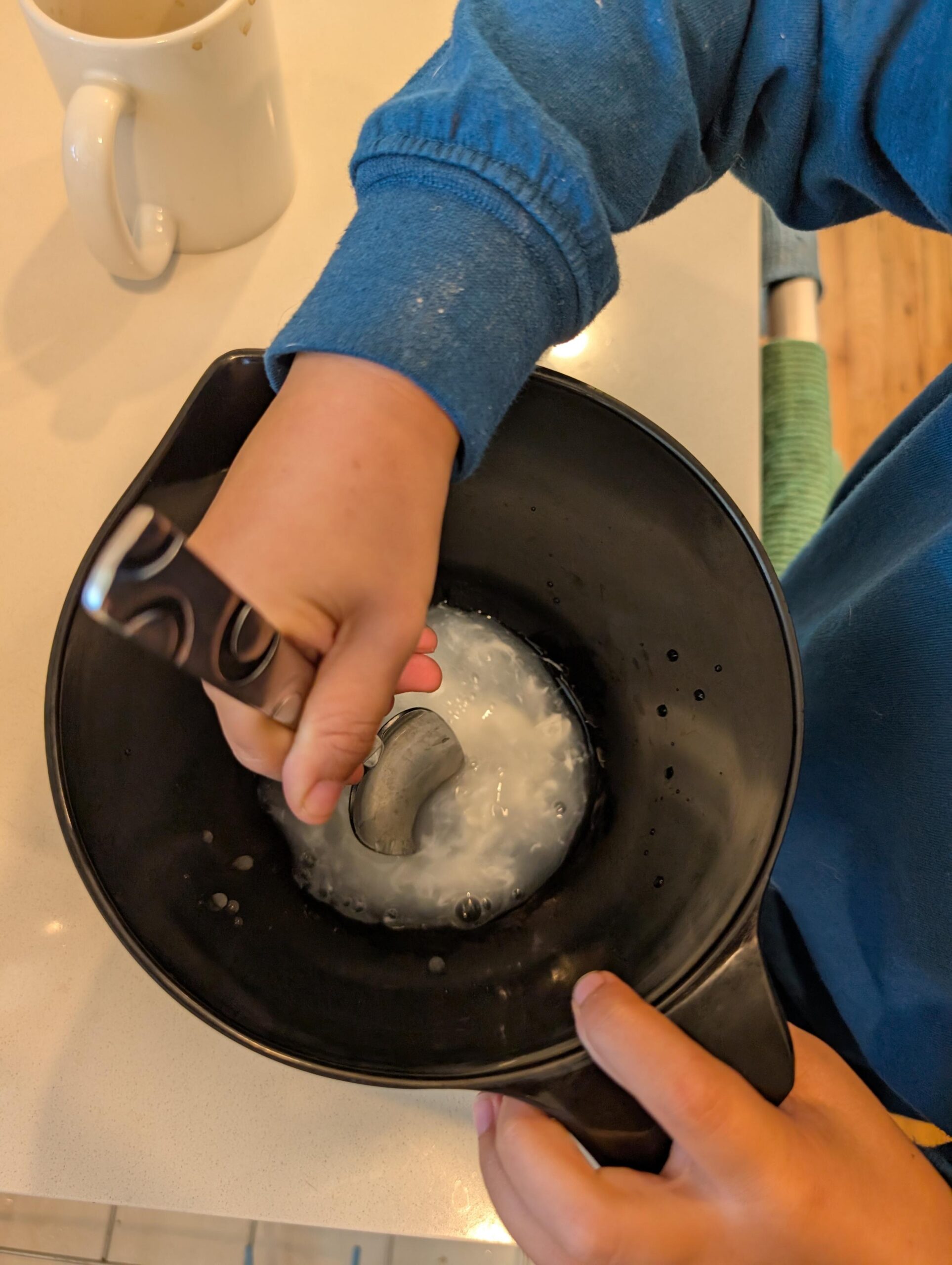 A black bowl with water and glue being mixed together by a child's hand