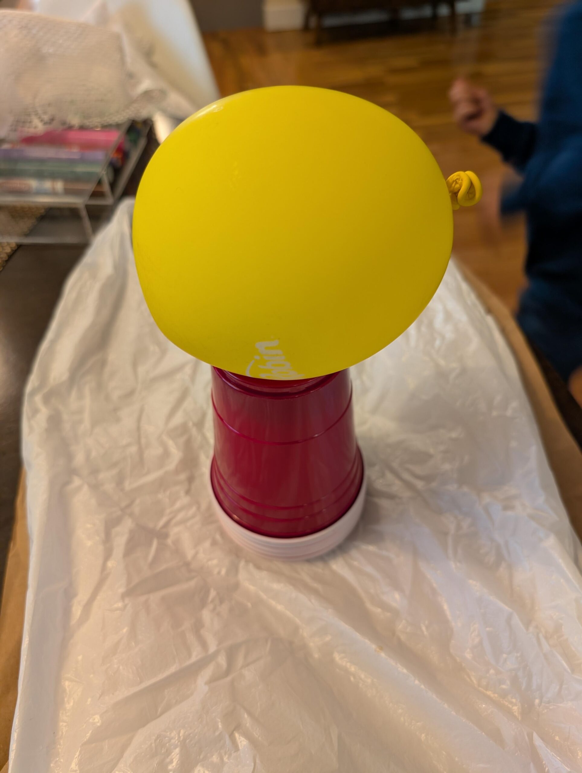 A small yellow balloon sitting on top of a stack of red solo cups