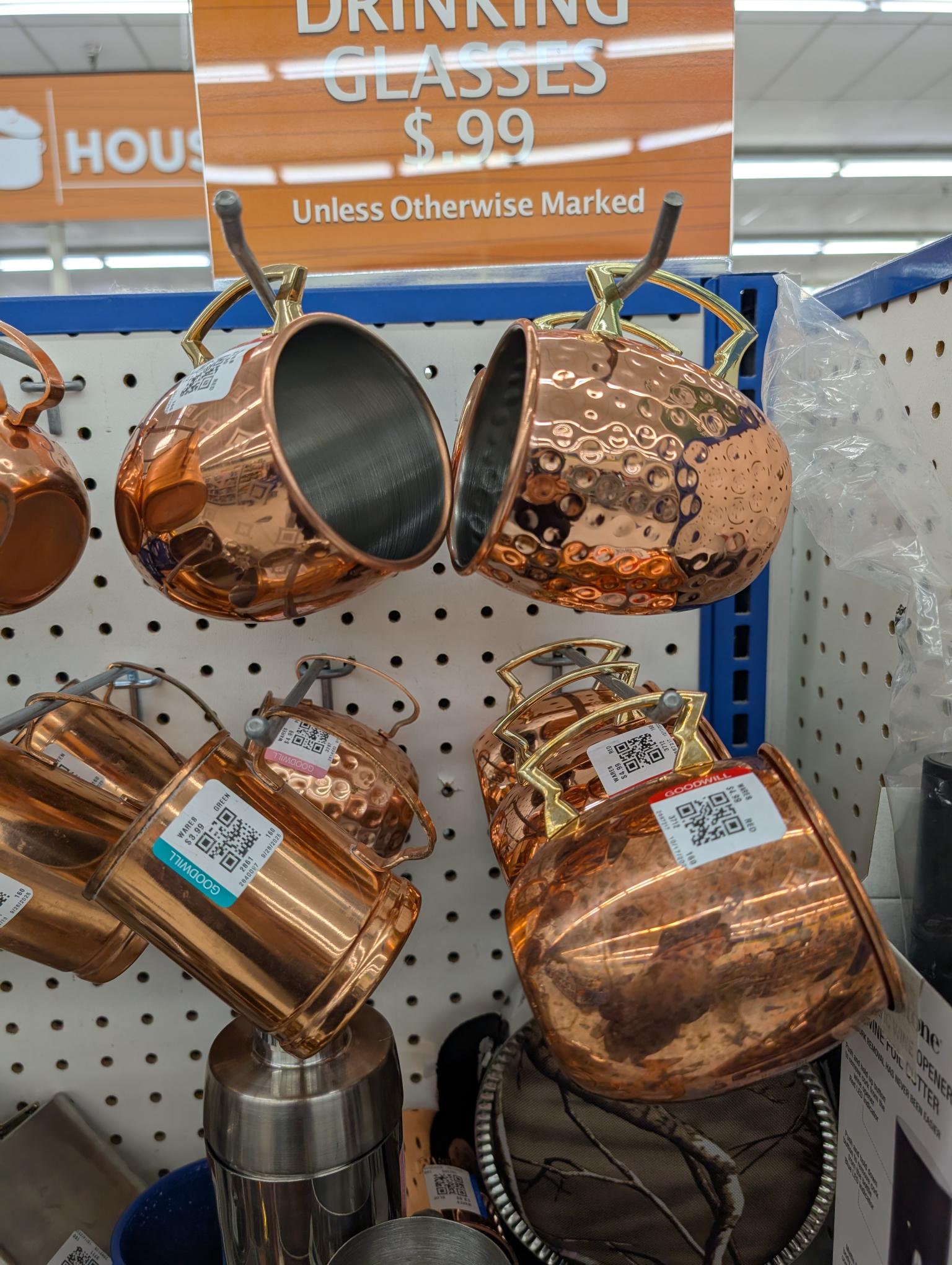 Copper mugs and cups hung up in the aisle of a Goodwill store.