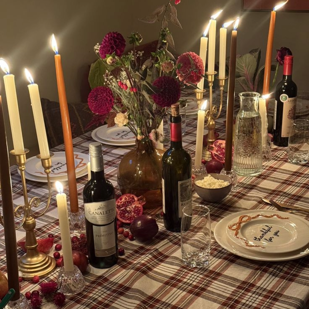 A DIY holiday tablescape with a plaid red and white tablecloth, tall candles, wine bottles, and flowers. 